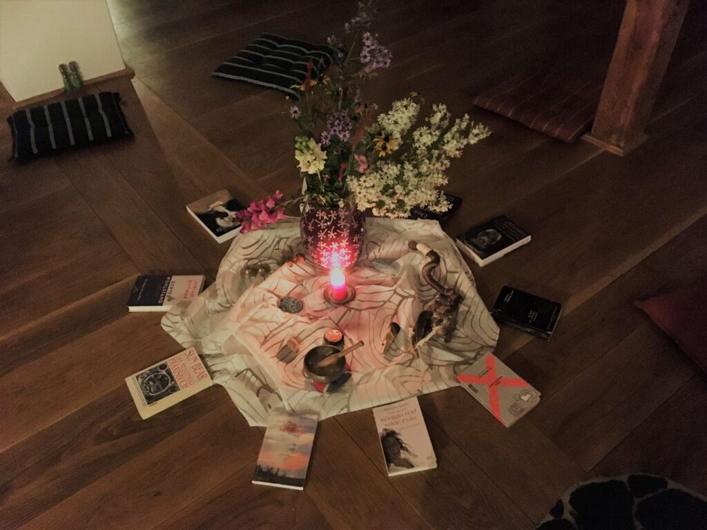 Kerze, Blumen und Bücher bilden eine Kreismitte.